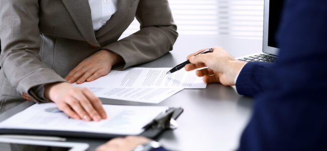 Business people and lawyer discussing contract papers sitting at the table, hands close-up. Teamwork or group operations concept.