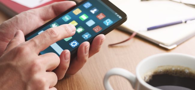 Closeup of male hands touching smartphone screen for using app at table.
