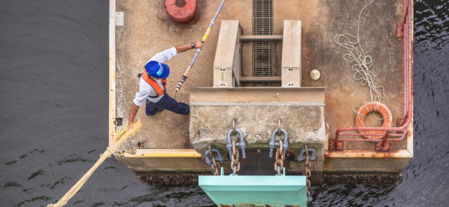 Dockworker hanging the mooring line of a ferry on a bollard of a pier with a boat hook.